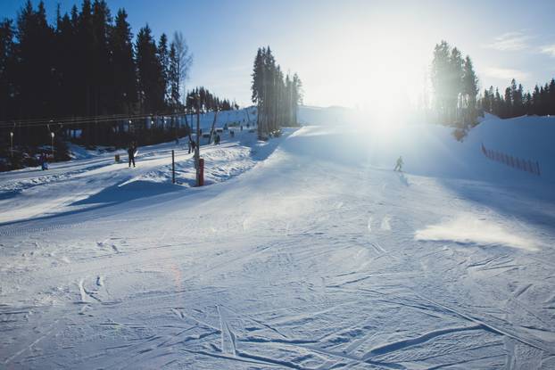 Beautiful cold mountain view of ski resort, sunny winter day with slope, piste and ski lift, with group of mountain downhill skiers and snowboarders