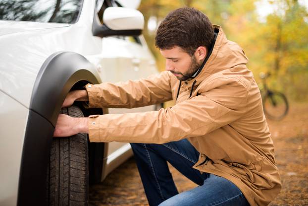 Young,Bearded,Man,Checking,Car,Tyre,In,Autumn,Forest