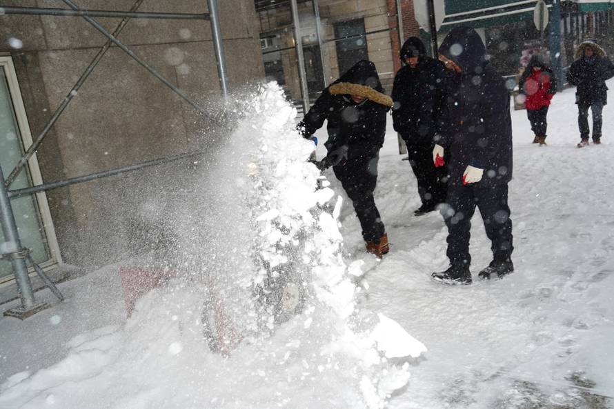 Workers use a snow blower to clear a sidewalk in Brooklyn