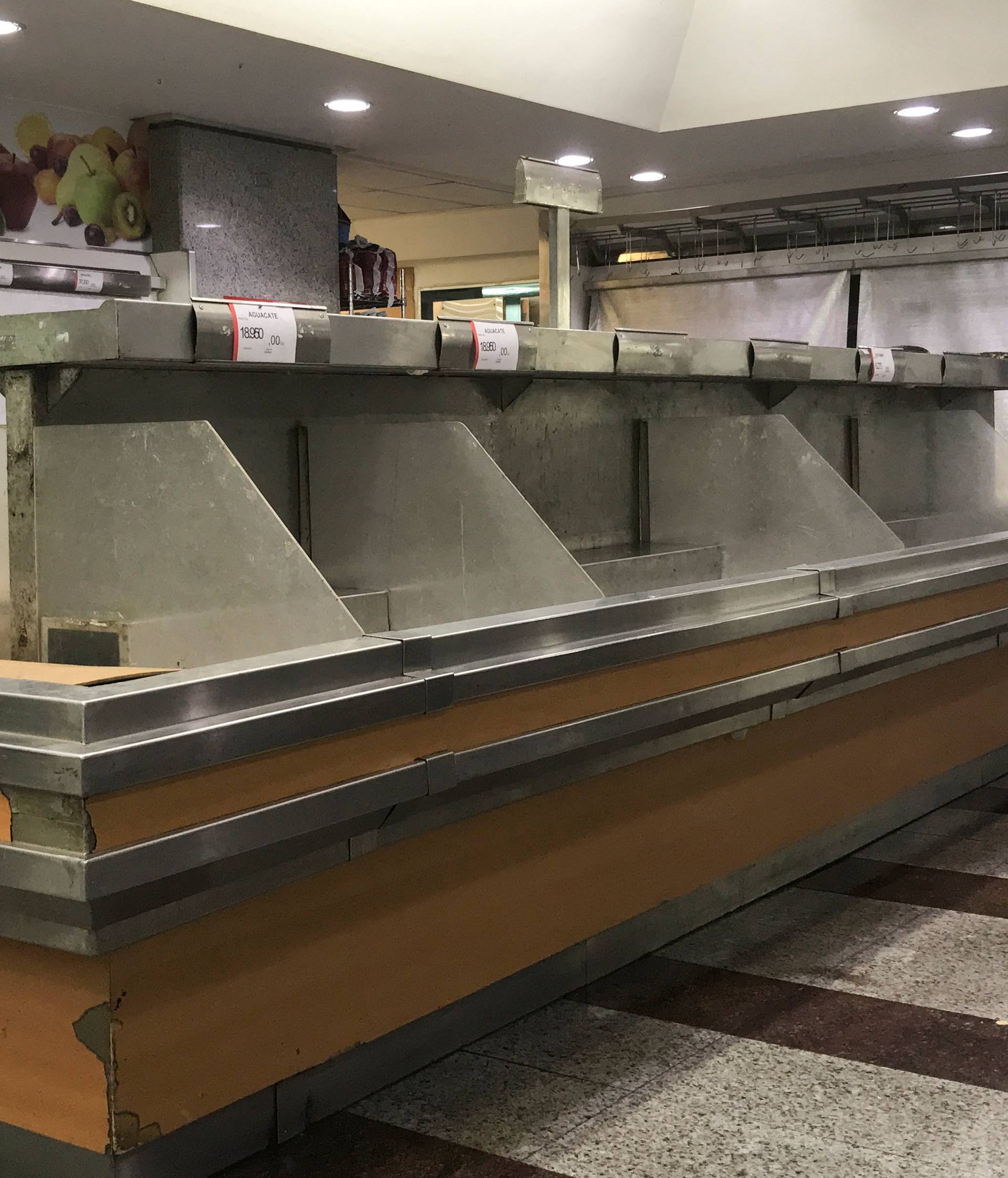 A woman walks past empty shelves at the fruits and vegetables area in a supermarket in Caracas
