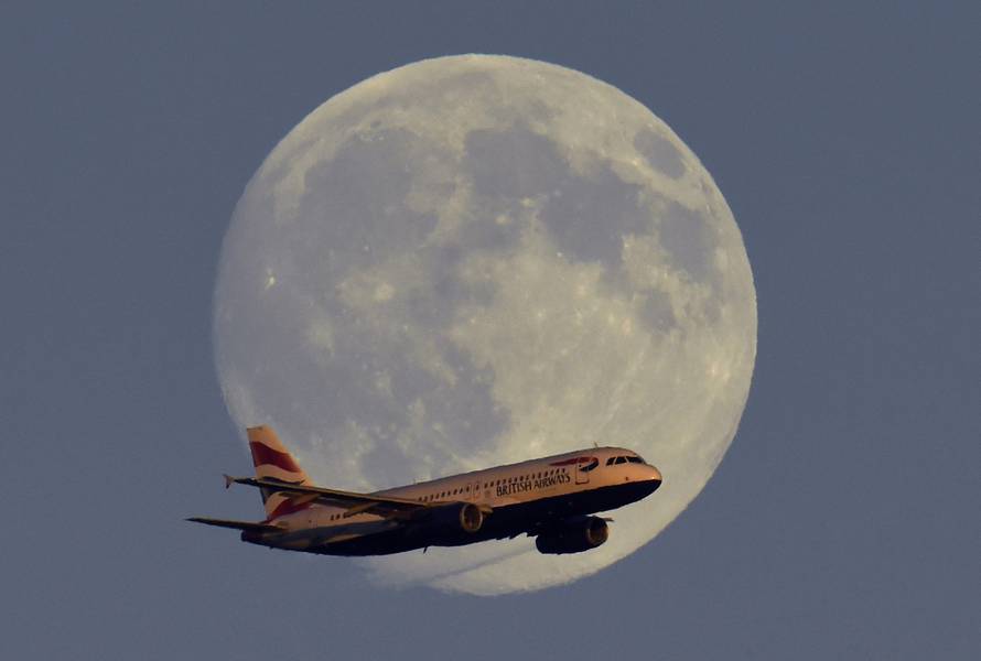 A British Airways passenger aircraft passes in front of the moon as it makes it's landing approach towards Heathrow Airport in west London in this photograph taken on July 18, 2016.