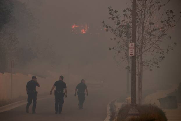 FILE PHOTO: Ventura policemen rush to check a home in a burning neighborhood as strong winds carry a wildfire into Ventura California