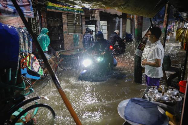 People ride rickshaws and motorcycle on a flooded street, amid continuous rain before the Cyclone Sitrang hits in Dhaka