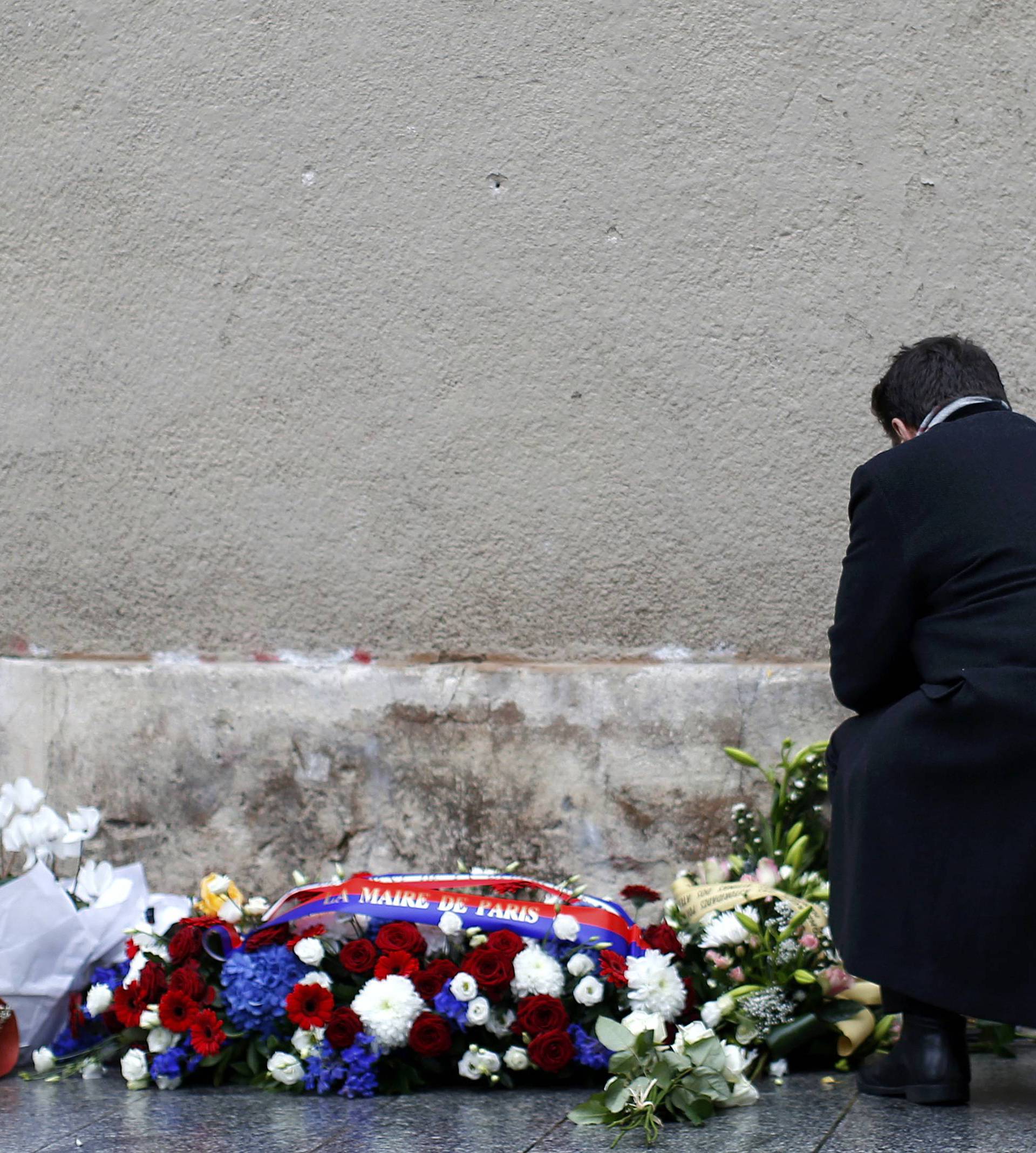 A man pays respects under a commemorative plaque unveiled by French President Francois Hollande and Paris Mayor Anne Hidalgo next to the "Le Carillon" and "Le Petit Cambodge" bars and restaurants in Paris