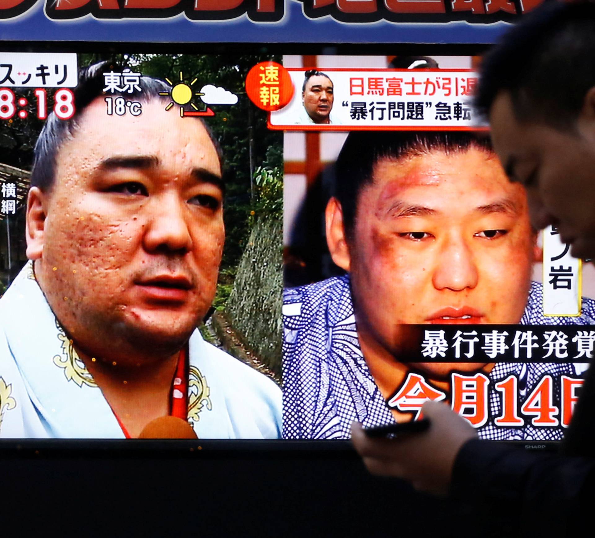 People walk past a street monitor showing Sumo grand champion Harumafuji (L) and junior wrestler Takanoiwa in Tokyo