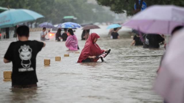 Residents wade through floodwaters on a flooded road amid heavy rainfall in Zhengzhou