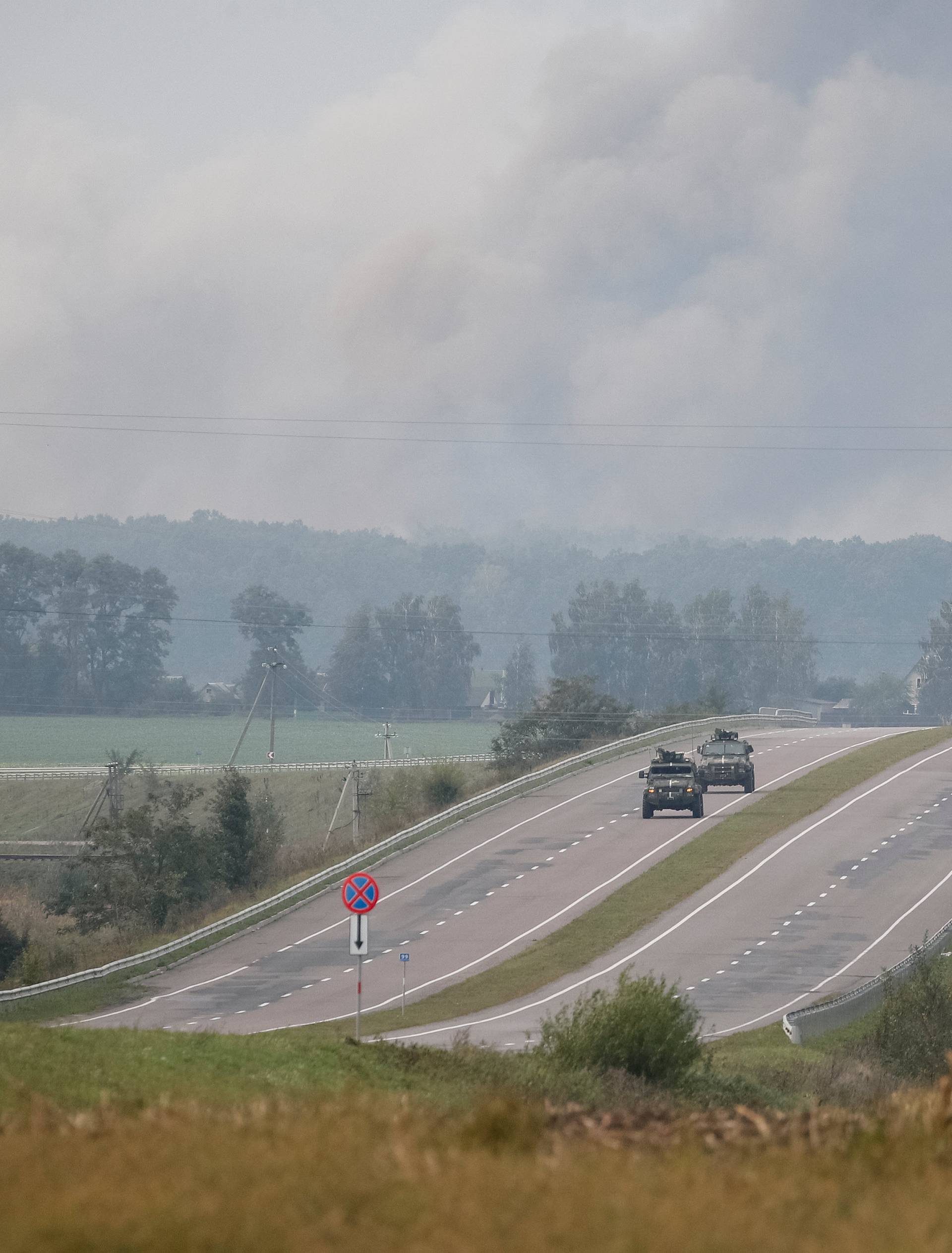 APC ride on the road as smoke rise over a warehouse storing ammunition for multiple rocket launcher systems at a military base in the town of Kalynivka