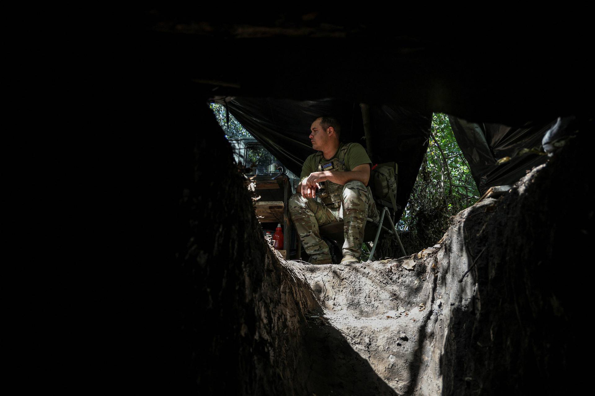 A Ukrainian serviceman sits in a chair, next to a dugout, at a position in a front line near the town of Bakhmut