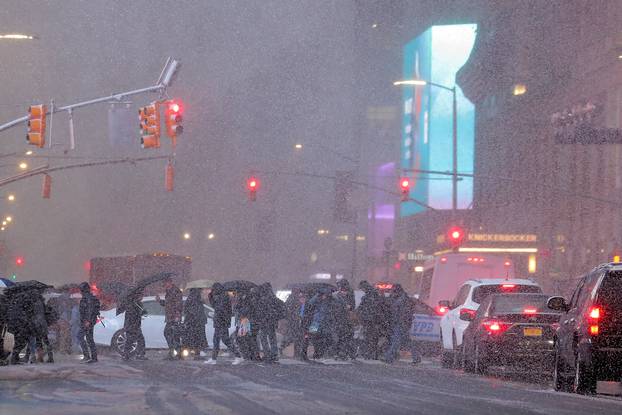 People walk through a snowstorm in Times Square during the evening commute in New York