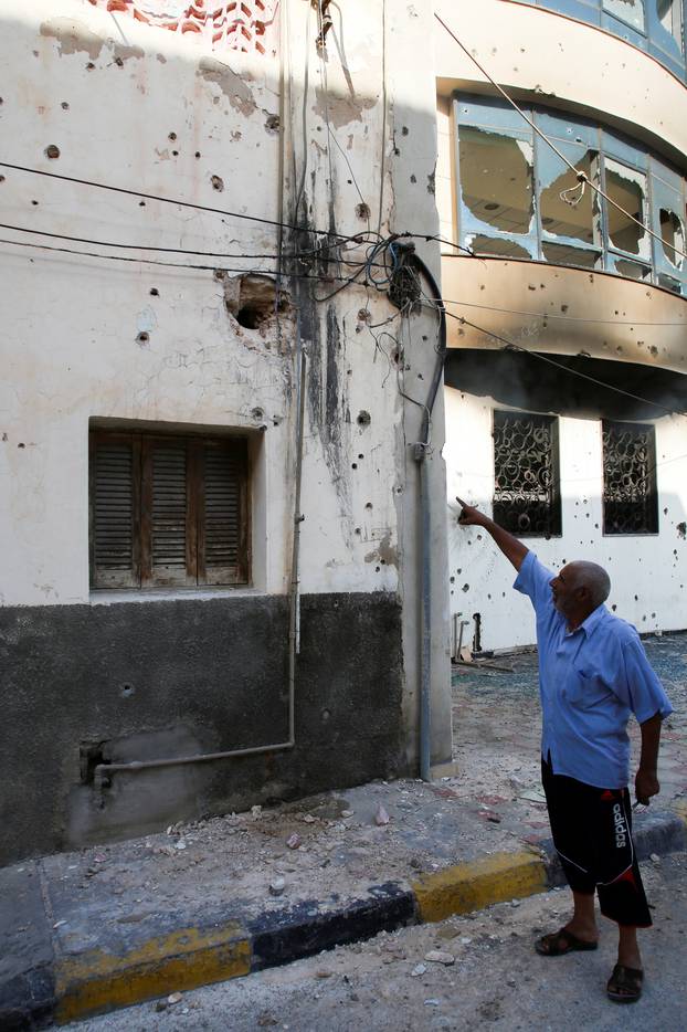 A man points at damages on a wall of a house after yesterday's clashes in Tripoli