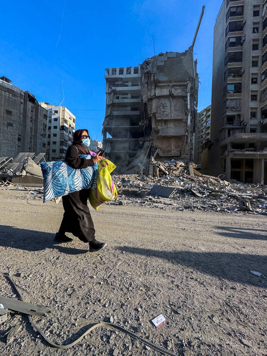 A woman walks past damaged buildings after an Israeli strike on Beirut's southern suburbs