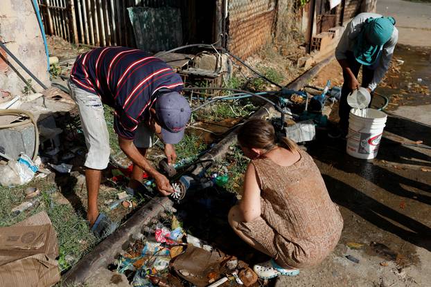 People set up a pump and fill buckets with water from a pipe in a street of Maracaibo