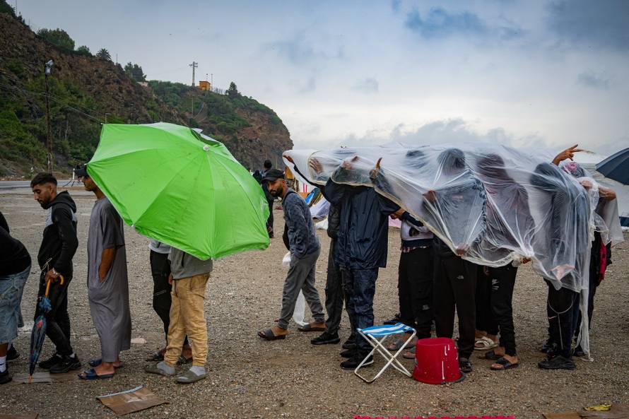 Migrants shield themselves from the rain while queuing to charge their mobile phones at an NGO stand in Ceuta