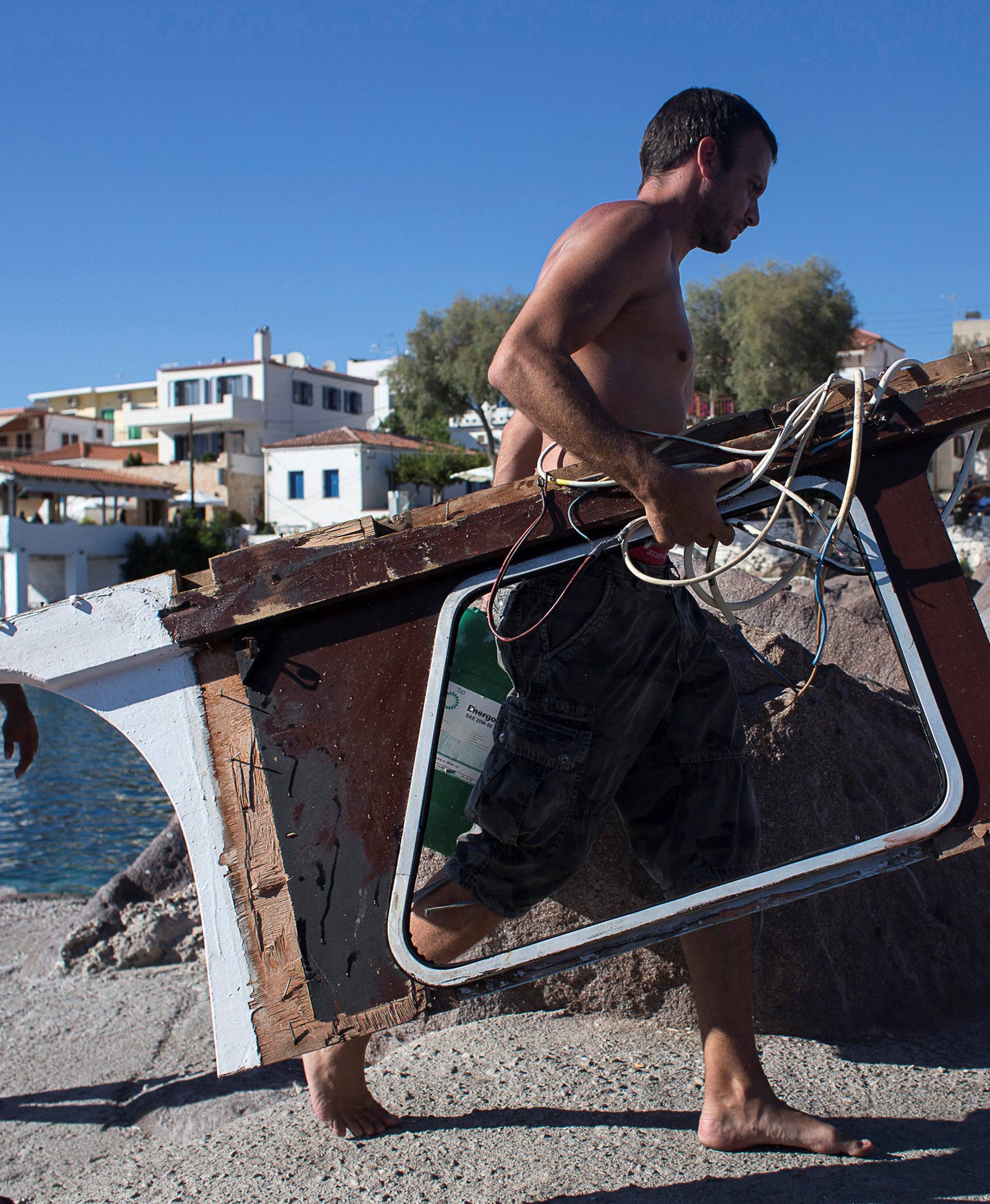 A man carrying a piece of boat, sunk by a speedboat,where four people, including a nine-year-old girl, died and at least five were injured off the Greek island of Aegina close to Athens