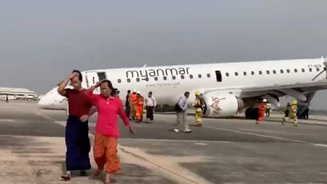 Passengers walk away from the plane after Myanmar National Airlines flight UB103 landed without a front wheel at Mandalay International Airport in Tada-u
