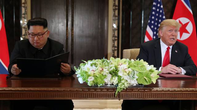 U.S. President Donald Trump speaks while North Korea's leader Kim Jong Un looks at the signed document, after their summit in Singapore