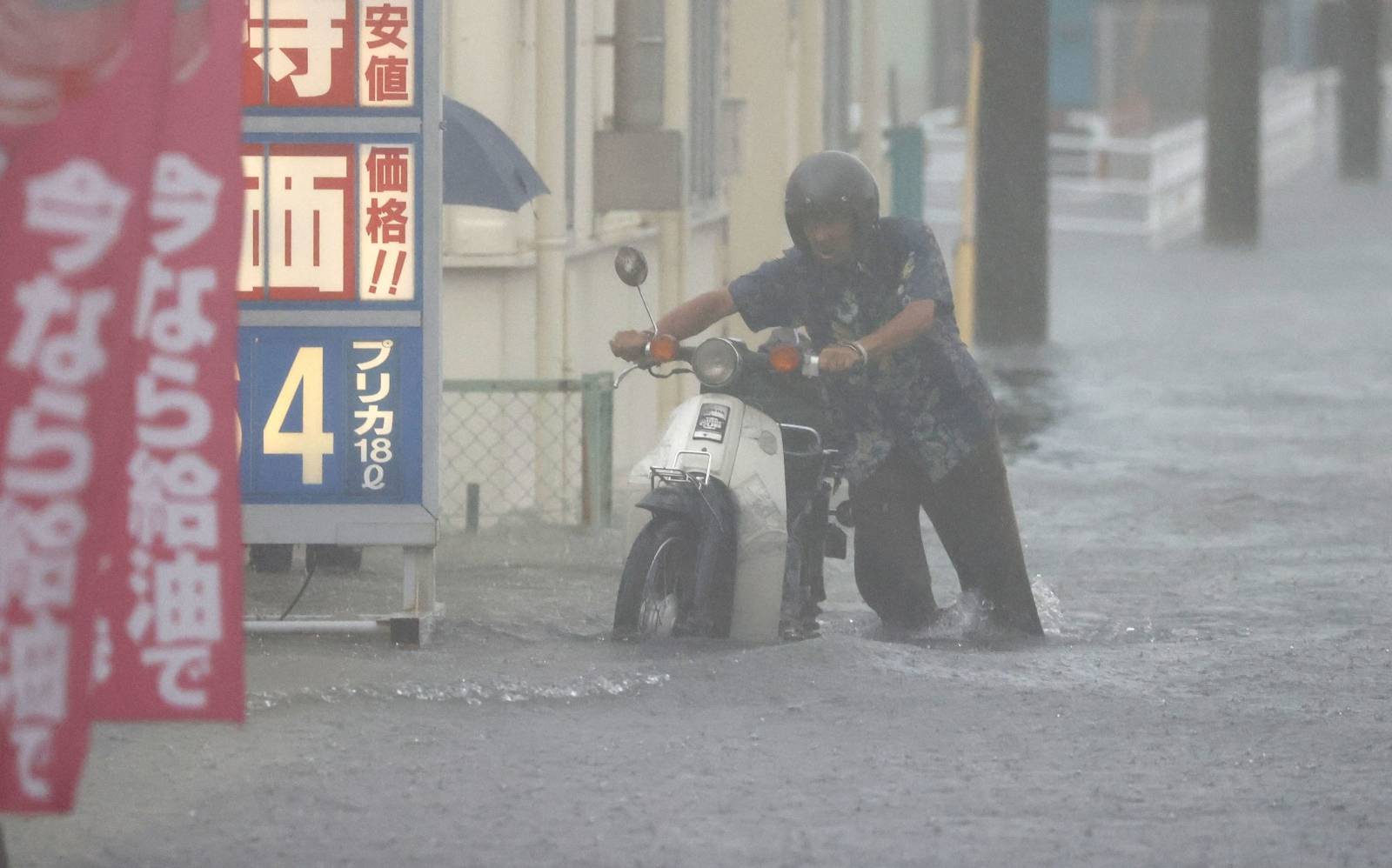 A man pushes a motorbike in a road flooded by heavy rain in Kurume, Japan