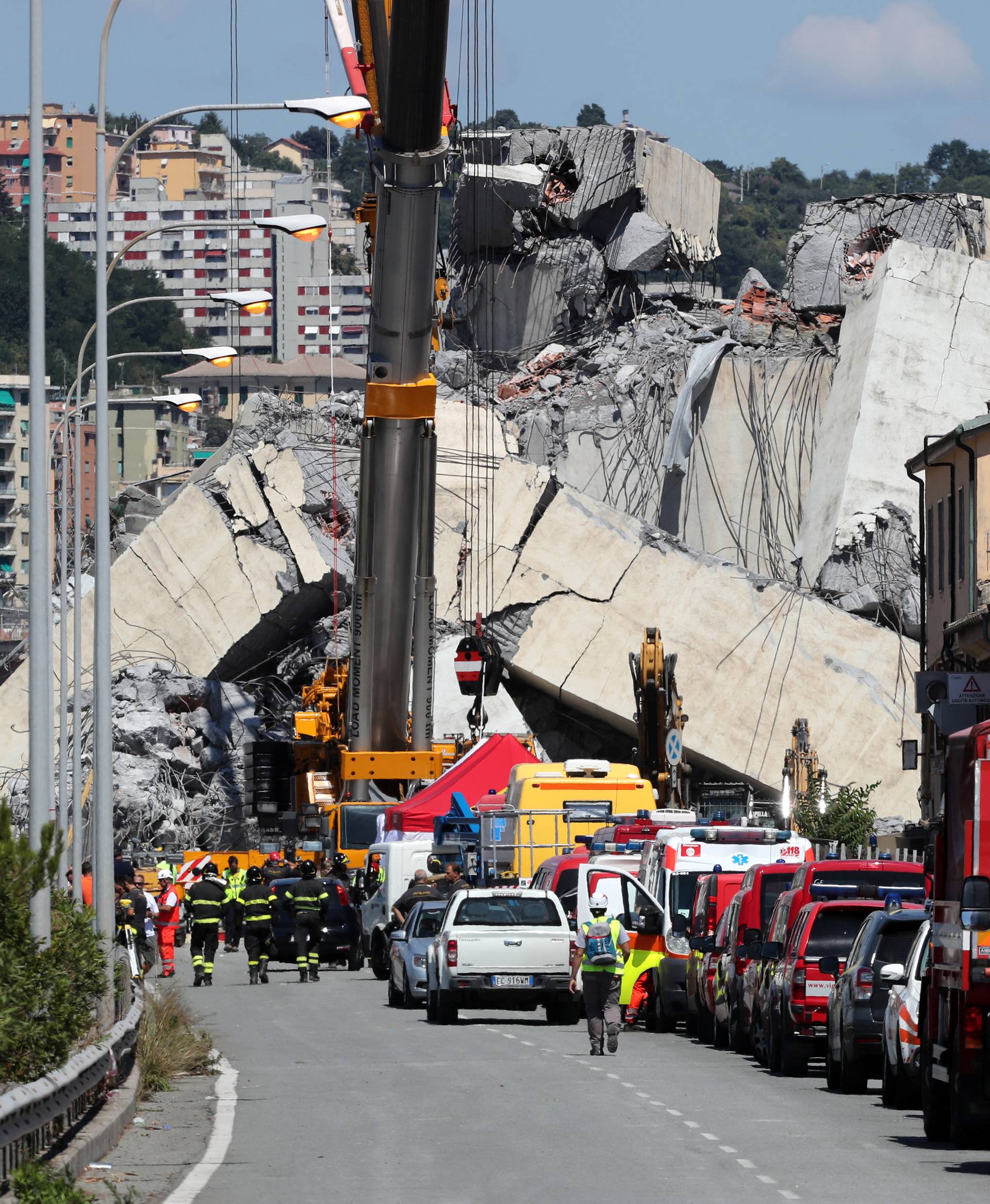 Firefighters and rescue workers stand at the site of a collapsed Morandi Bridge in the port city of Genoa
