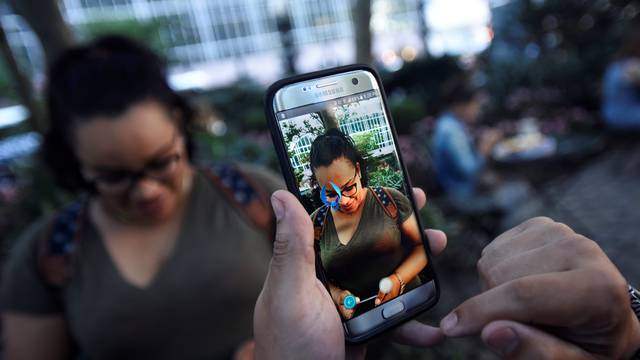 A Pokemon appears on the screen next to a woman as a man plays the augmented reality mobile game "Pokemon Go" by Nintendo in Bryant Park in New York City