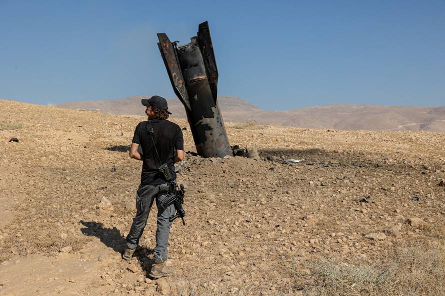 An Israeli settler stands next to part of a missile protruding from the ground, following strikes from Iran, in the central Israeli-occupied West Bank