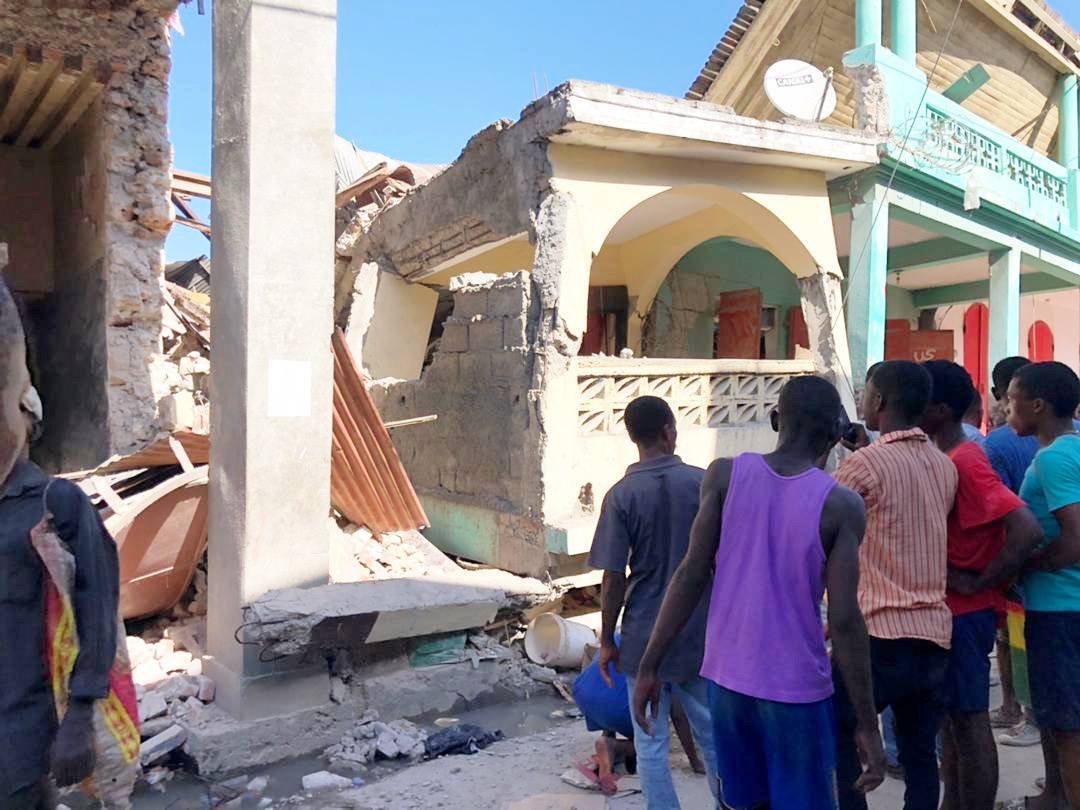 People stand in front of collapsed buildings following an earthquake in Jeremie