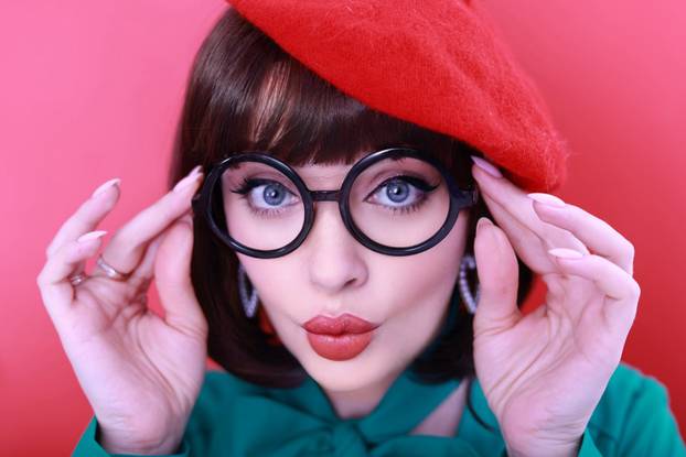 Young happy woman 30 years old wearing glasses, she wears a green grunt and a red hat, shows emotions, celebrates,