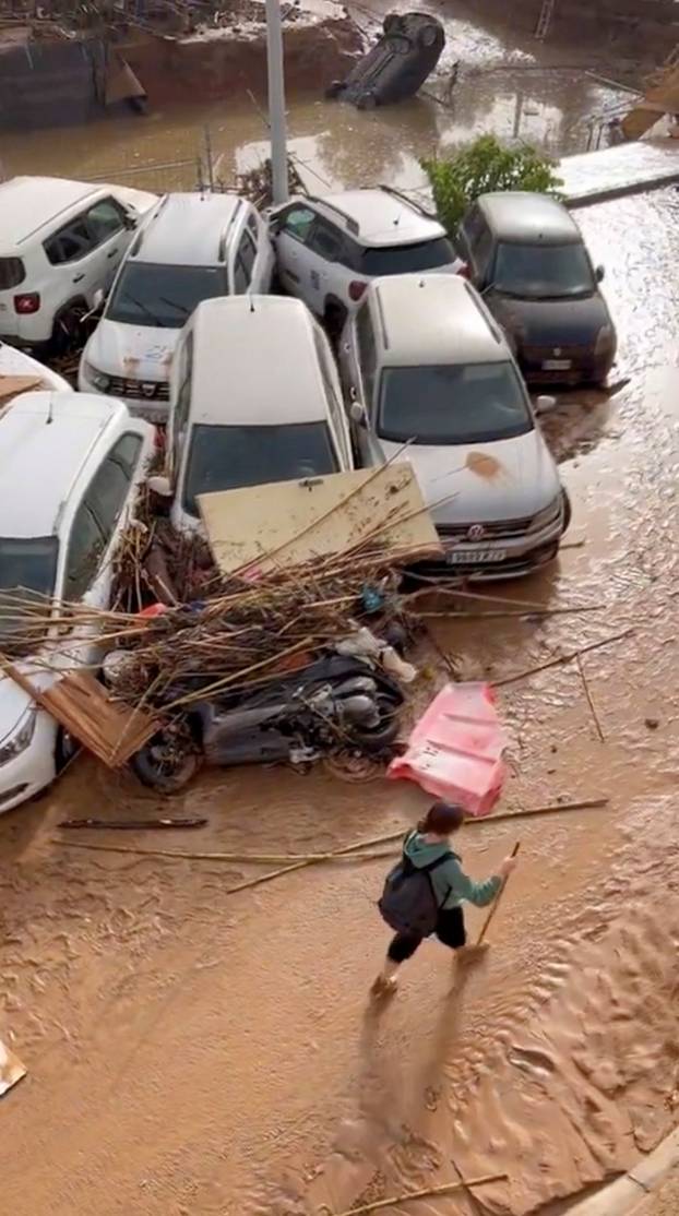 A person walks past vehicles piled with debris after torrential rains and flooding in Paiporta, Valencia