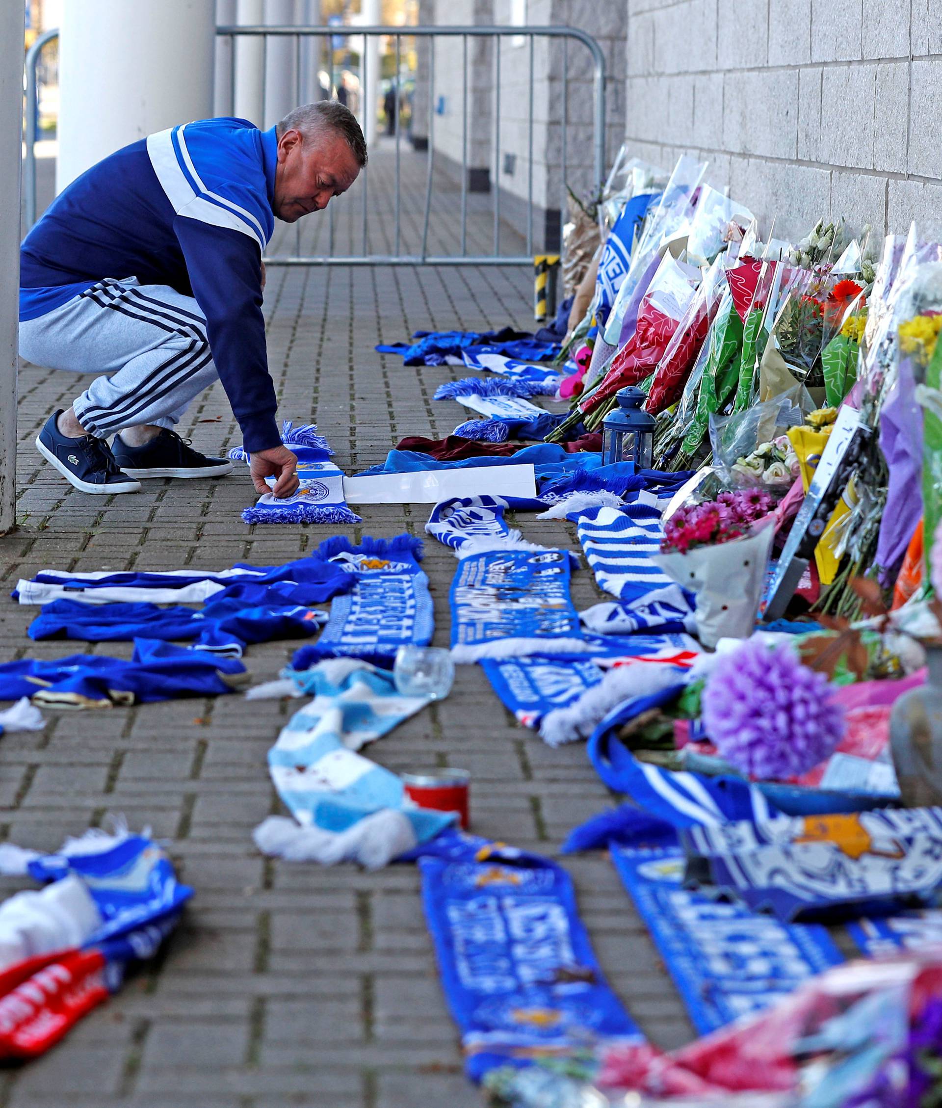 A Leicester City football fan places a scarf outside the football stadium, after the helicopter of the club owner Thai businessman Vichai Srivaddhanaprabha crashed when leaving the ground on Saturday evening after the match, in Leicester