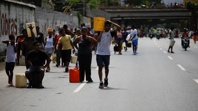People walk on a highway, carrying containers with water collected from a sewage drain in Caracas
