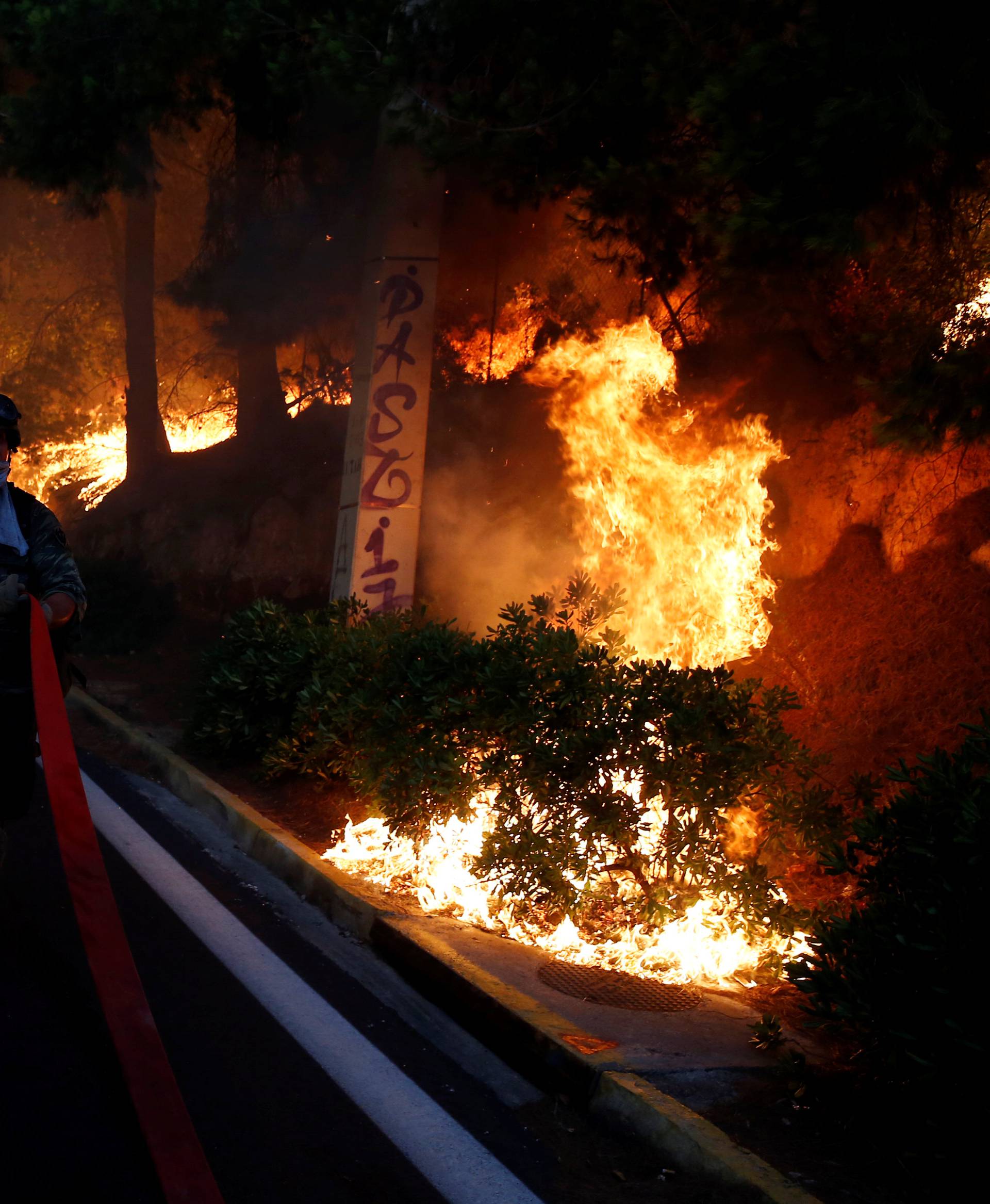 A soldier holds a hose as a wildfire burns in the town of Rafina, near Athens