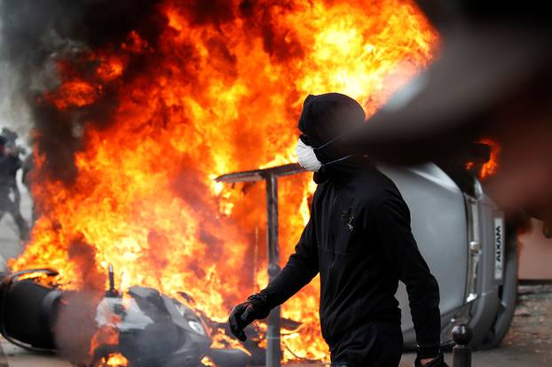 A masked protester walks near a car that burns outside a Renault automobile garage during clashes during the May Day labour union march in Paris