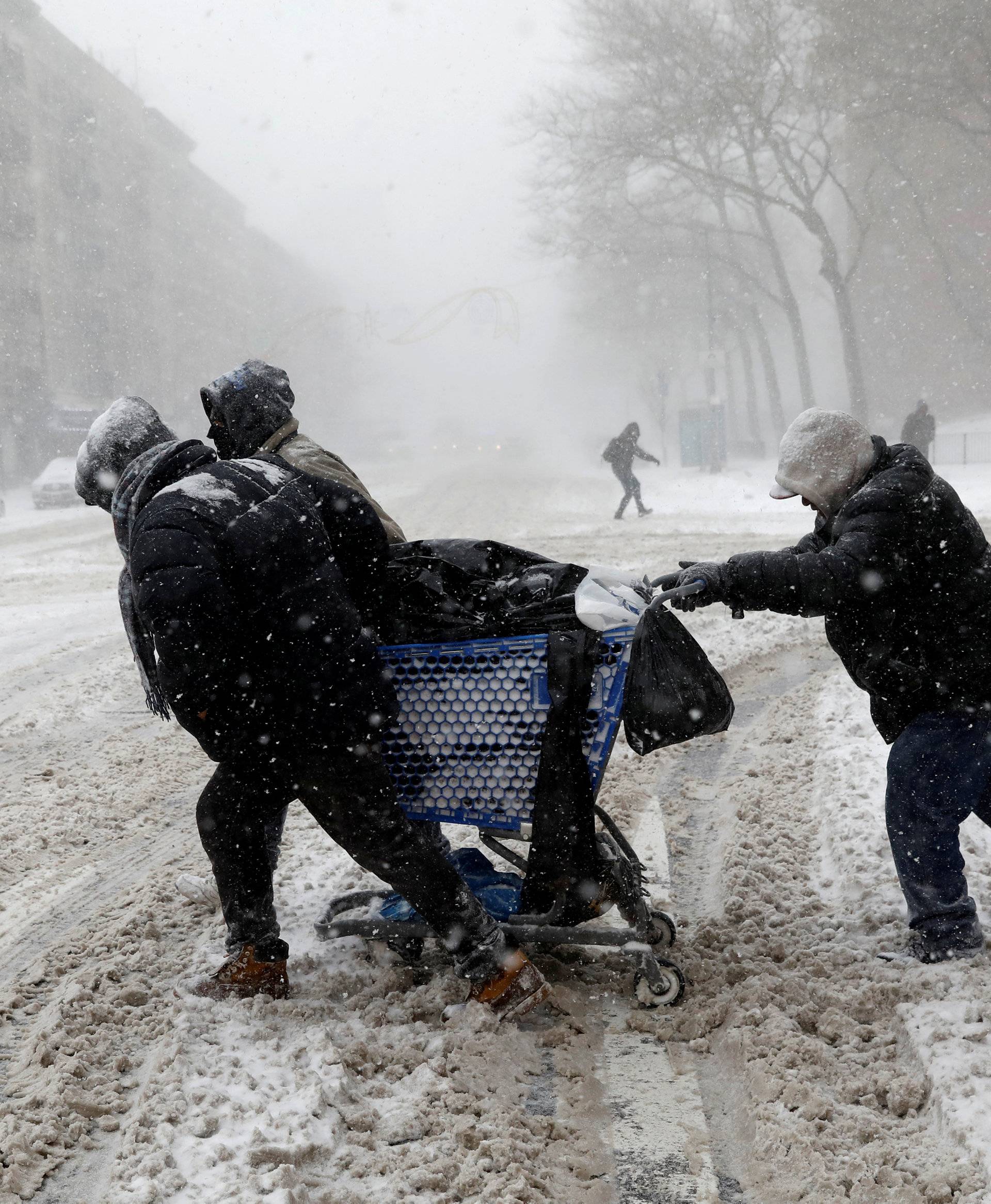 Men struggle against wind and snow as they push a shopping cart across 125th street in upper Manhattan during a snowstorm in New York City