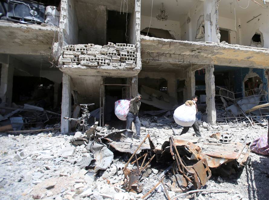 People hold belongings as they walk on the rubble of damaged buildings in the city of Douma, Damascus