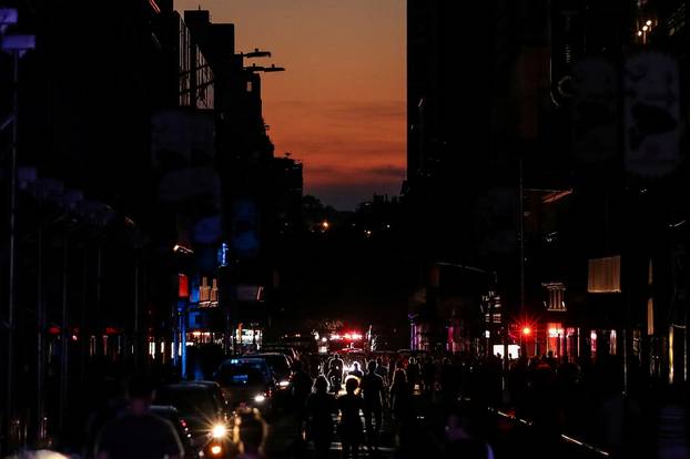 People walk along a dark street near Times Square area, as a blackout affects buildings and traffic during widespread power outages in the Manhattan borough of New York