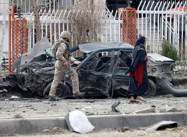 A member of Afghan security forces inspects a damaged vehicle at the site of a blast in Kabul