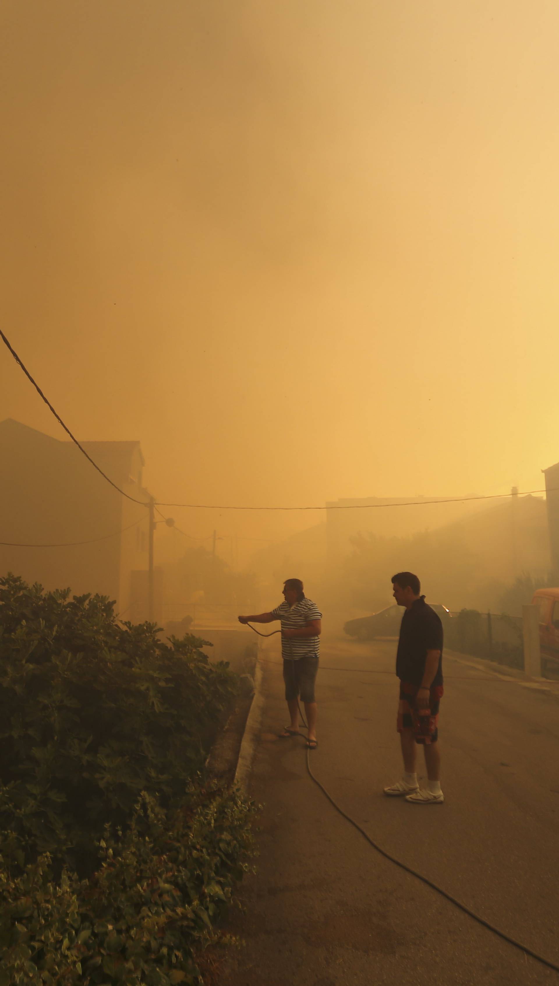 Local residents stand amid smoke as they leave their homes due to a wildfire in the village of Mravinc near Split