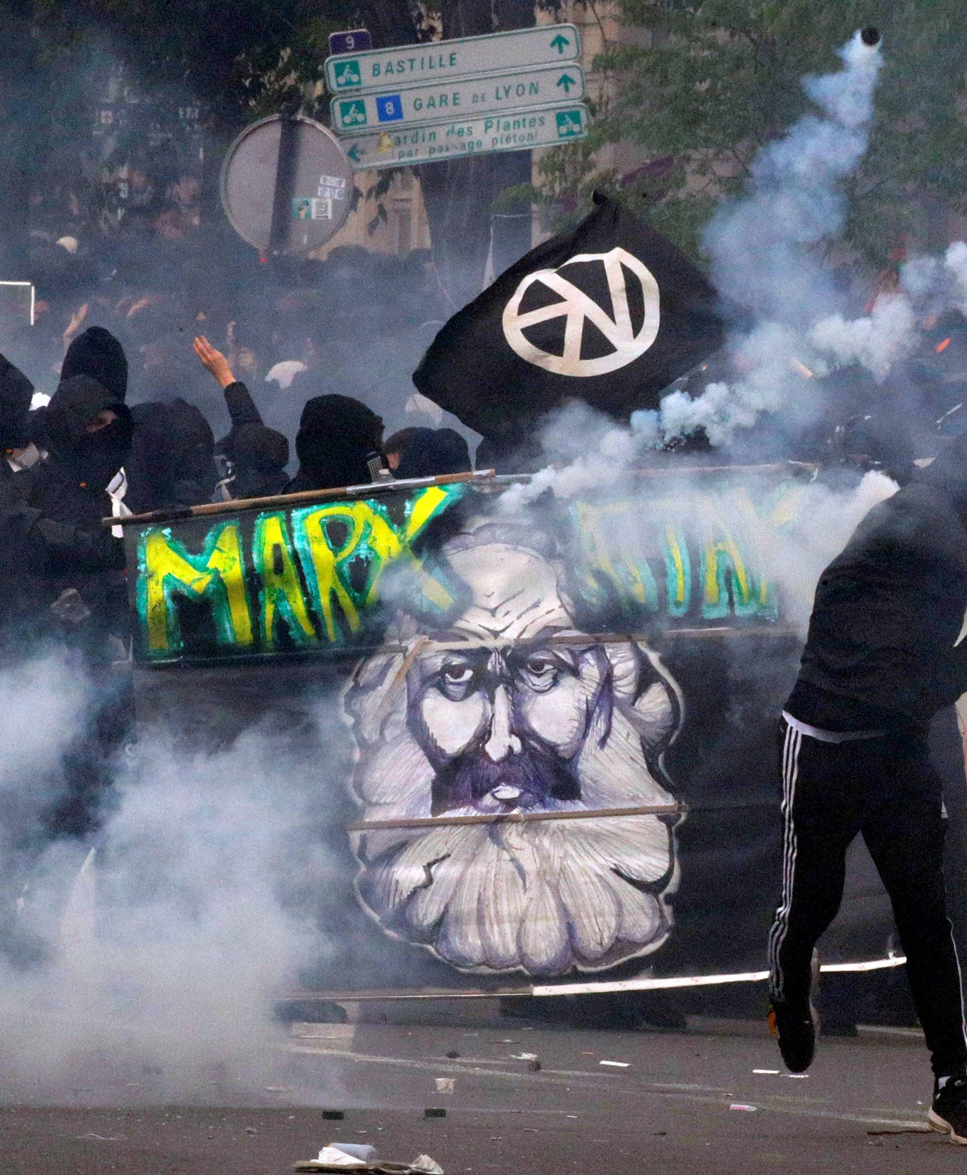 Tear gas floats around masked protesters during clashes with French CRS riot police at the May Day labour union rally in Paris