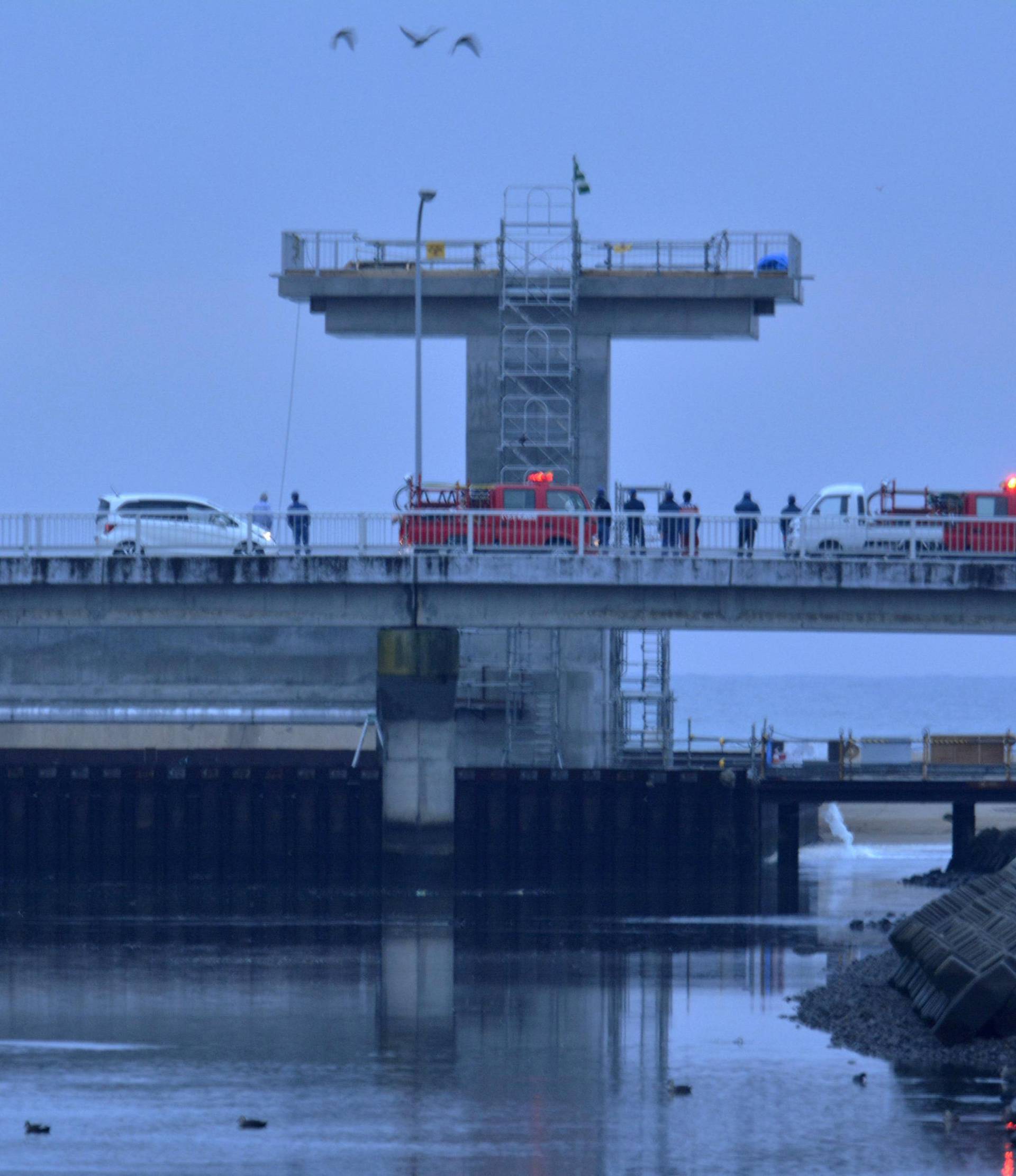 People keep a lookout at the mouth of a river after tsunami advisories triggered by an earthquake were issued, in Iwaki, Fukushima prefecture, Japan