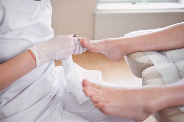 Professional medical pedicure procedure close up using nail clippers instrument. Patient visiting chiropodist podiatrist. Foot treatment in SPA salon. Podiatry clinic. Pedicurist hands white gloves.