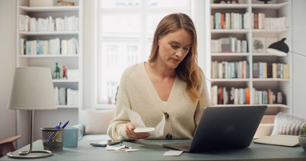 White,Woman,In,Cream,Cardigan,Reviews,Receipts,At,Her,Laptop.
