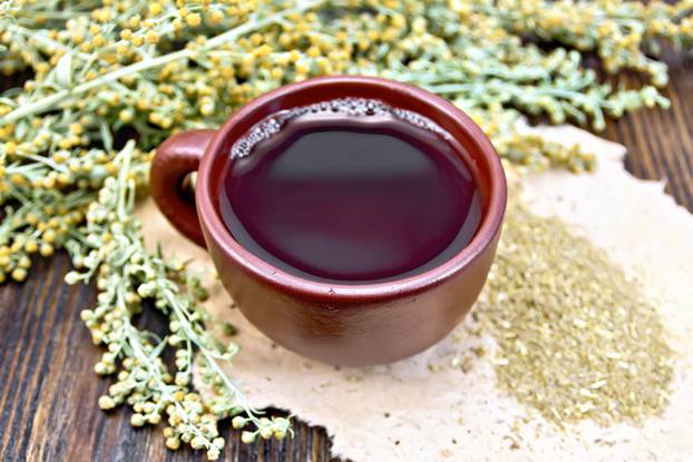 Tea with wormwood in brown cup on dark board