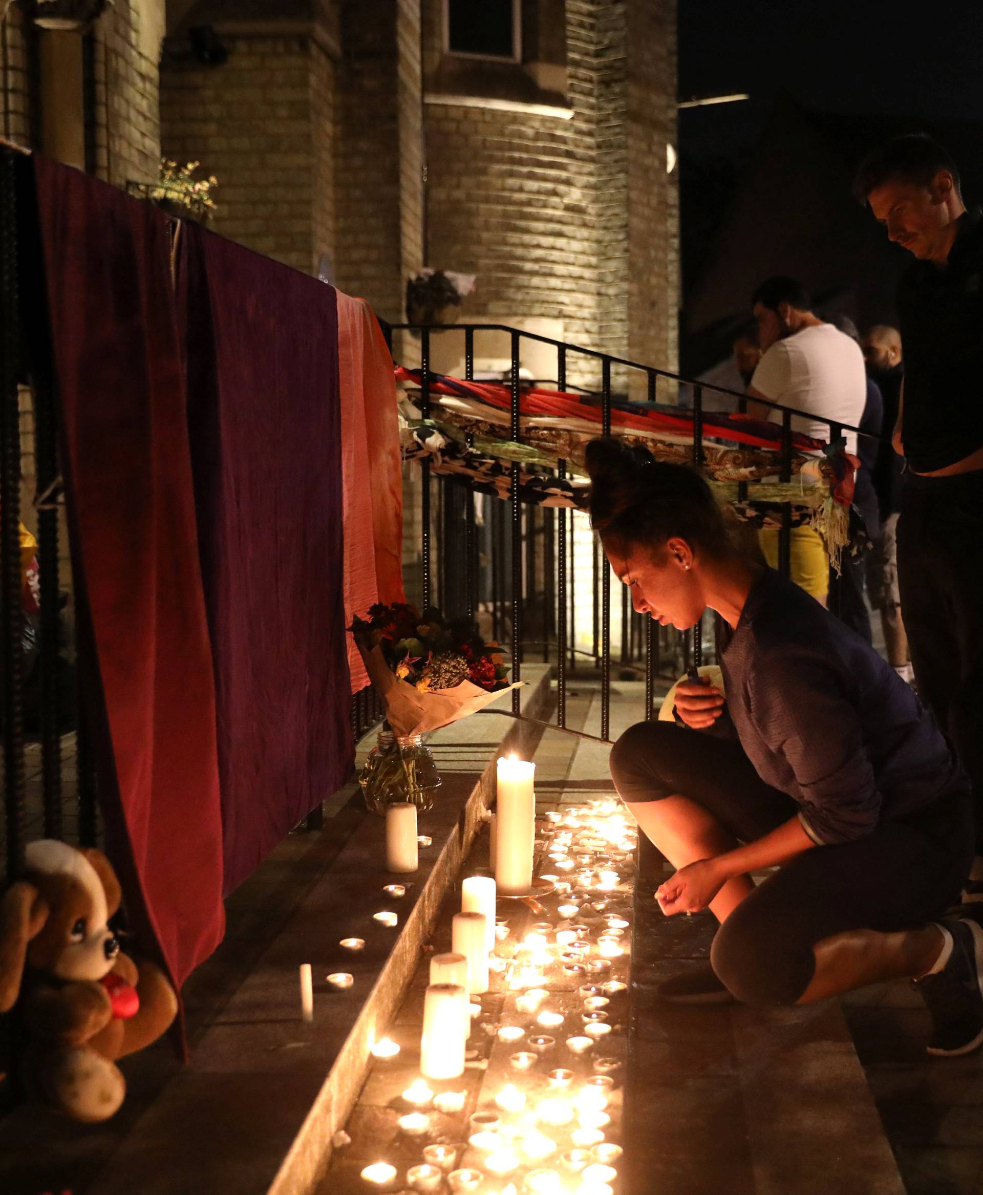 A woman lights a candle outside a church near a tower block severely damaged by a serious fire, in north Kensington, West London