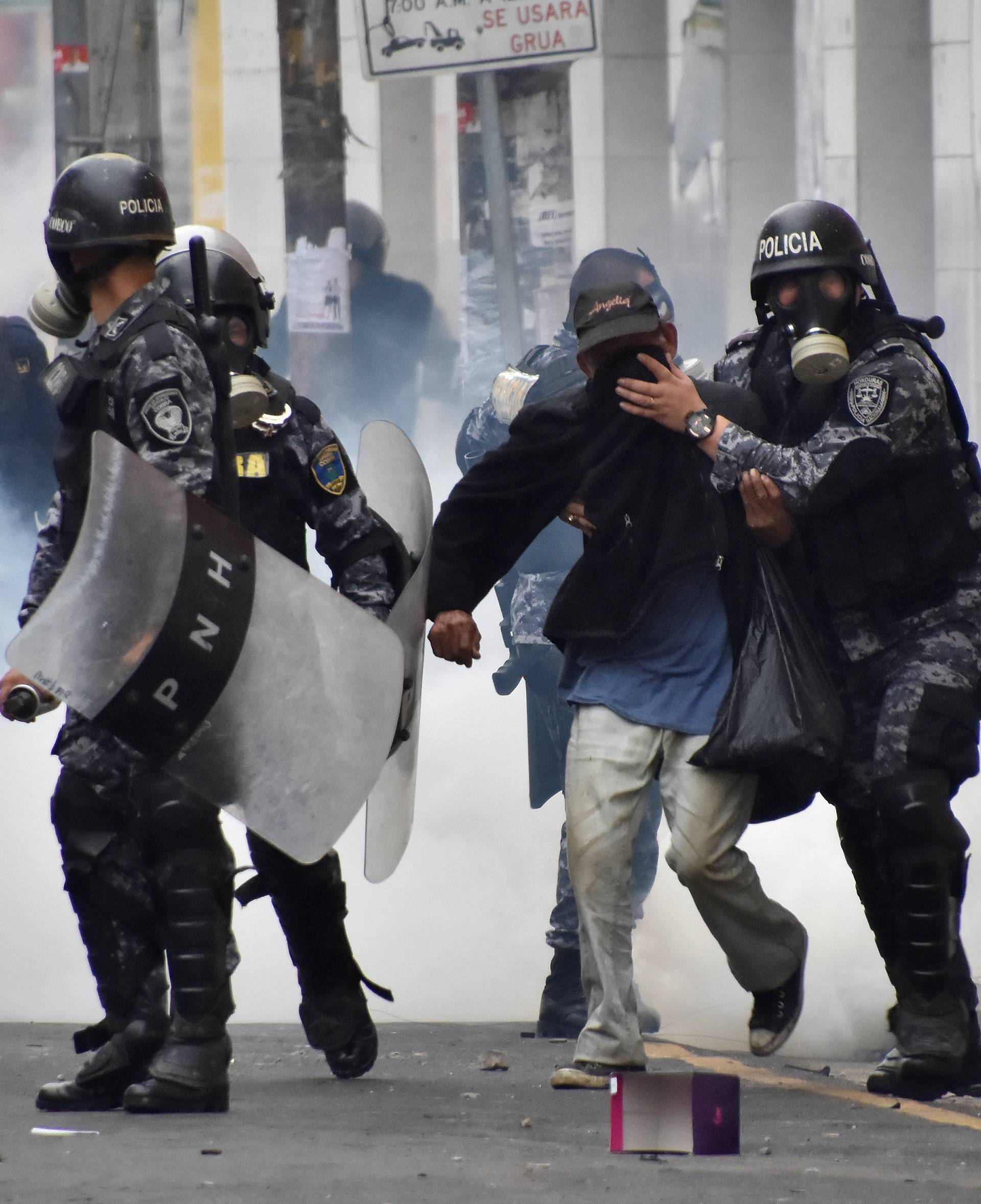Police help a pedestrian overcome by tear gas as supporters of Nasralla clash with police during a protest caused by the delayed vote count for the presidential election in San Pedro Sula