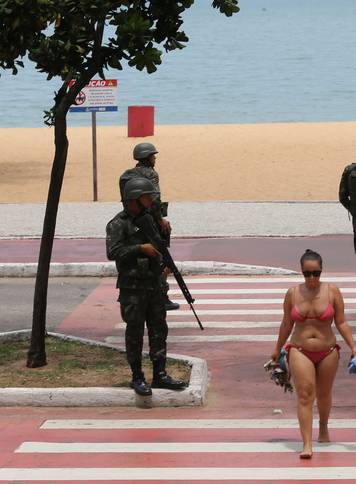 A woman walks as army soldiers patrol at Costa beach in Vitoria