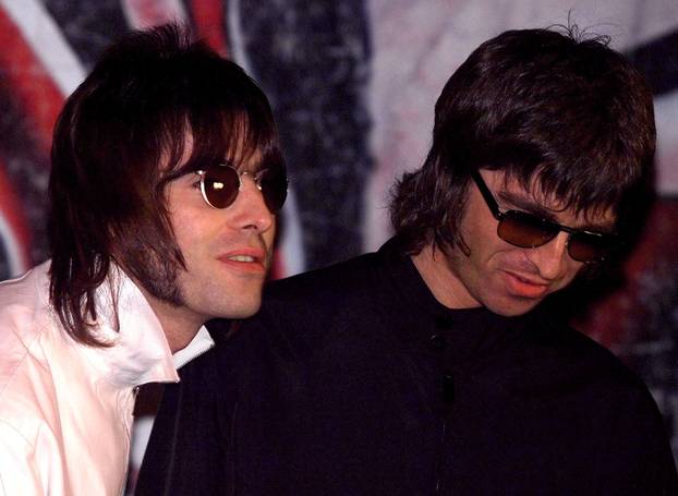 FILE PHOTO: Liam and Noel (R) Gallagher, of the British rock band Oasis, wait for the start of a news conference at a pub in London