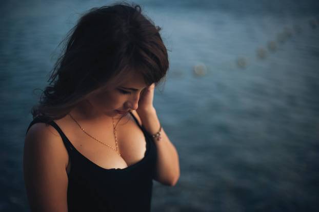 Sexy young woman in the black dress posing by the sea