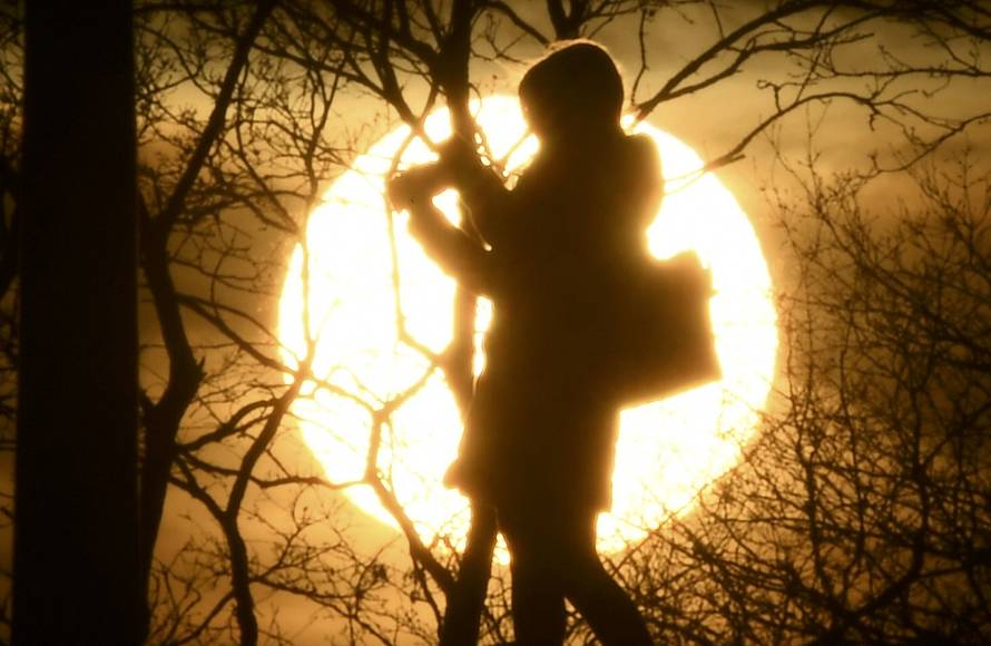 A woman takes photographs in front of the setting sun on Primrose Hill in London