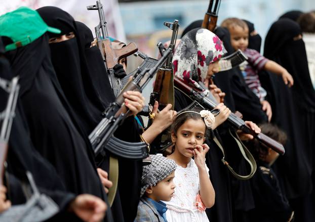 Girl looks at armed women loyal to the Houthi movement as they take part in a parade to show support for the movement in Sanaa, Yemen
