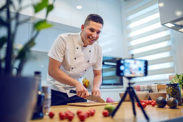 Smiling,Caucasian,Chef,In,Uniform,Standing,In,Kitchen,And,Cutting