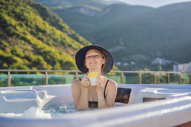 Portrait of young carefree happy smiling woman relaxing at hot tub during enjoying happy traveling moment vacation life against the background of green big mountains